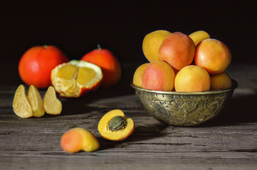 Delicious fresh apricots placed in copper bowl with fresh tangerine on rustic wooden background.Close up