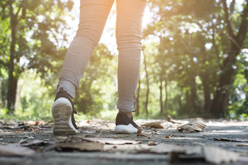 Lonely woman wearing jeans and black sneakers walking along the path in the park.
