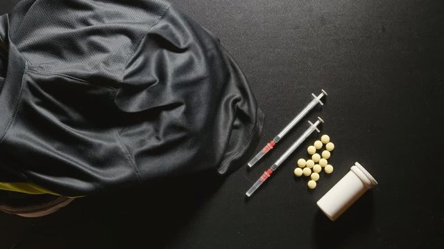 DOPING: Sport t-shirt falls on a sneakers near a pills and syringe - slow motion, top view