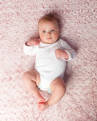 Laying newborn baby girl with white bodysuit on blanket. View from above.