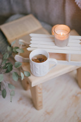 Still life details of interior: knitted clothes on a vintage wooden floor, cup of tea, candles and book