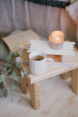 Still life details of interior: knitted clothes on a vintage wooden floor, cup of tea, candles and book