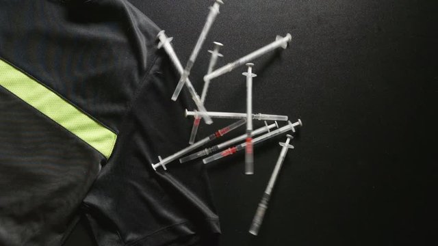 DOPING: Syringes fall on a sport T-shirt - slow motion, top view