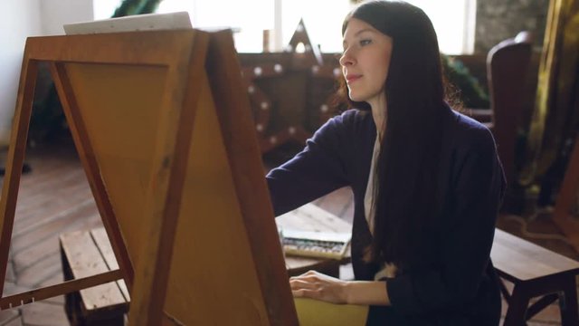 Young woman artist draw pictrure with watercolor paints and brush on easel canvas