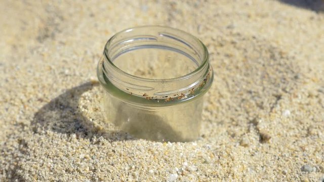 hand of man throwing cigarette in a glass jar in the sand
