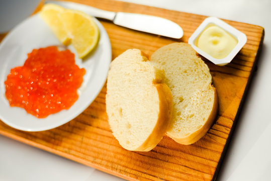 Red caviar with lemon, bread and butter on wooden board white table background. Close up image of delicacy food luxury lifestyle