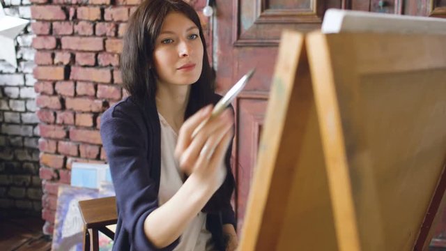 Young woman artist draw pictrure with watercolor paints and brush on easel canvas