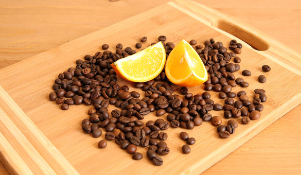 A pile of coffee beans on a board with a couple of orange lobules