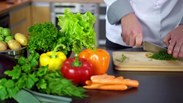 chef chopping dill on wooden board in kitchen