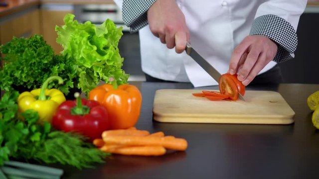 chef cutting tomato on board in kitchen
