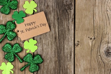Happy St Patricks Day tag with side border of shiny shamrocks over a rustic wood background