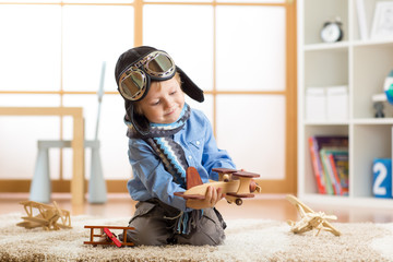 Little kid boy dreams be an aviator and plays with toy airplanes sitting on floor in nursery room