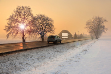 Samochód na drodze w zimowym krajobrazie o wschodzie słońca.
