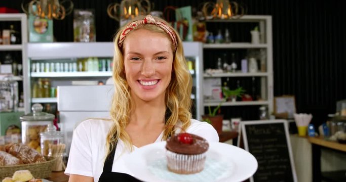 Portrait of smiling waitress holding a plate with a cupcake in cafÃ© 4k