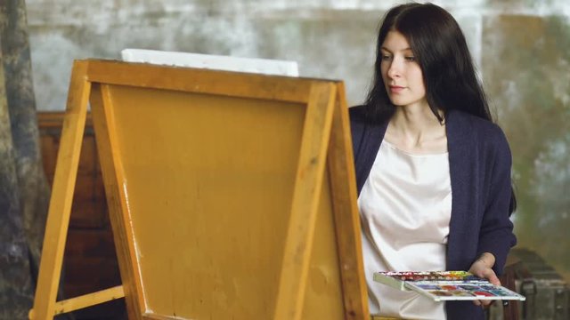 Young woman artist draw pictrure with watercolor paints and brush on easel canvas
