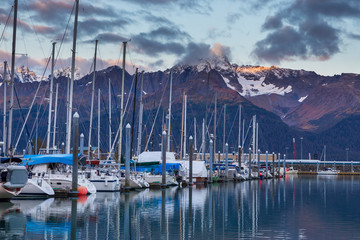 Fototapeta na wymiar Boats at a pier in Seward with mountains in background. Seward's Boat Harbor is situated on the northern edge of Resurrection Bay.