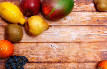 Fruits on a wooden background. Mango, kiwi, tangerine, lemon, pear, grape, persimmon, apple.