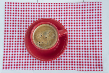 red cup of coffee on checkered napkin and white wooden background