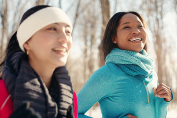Multi-ethnic pair of female friends taking a break from jogging in the snow in winter
