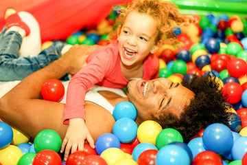Young father playing with his daughter inside ball pit swimming pool