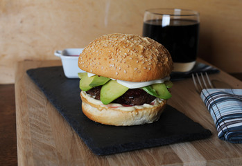 Burger, beer and berry sauce in white gravy boat on a slate base, glass and cutlery served on a wooden board,