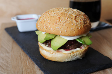 Burger, beer and berry sauce in white gravy boat on a slate base, glass and cutlery served on a wooden board,