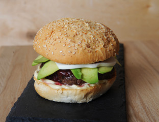 Burger closeup on a slate base, glass and cutlery served on a wooden board