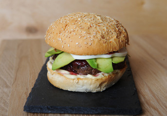 Burger closeup on a slate base, glass and cutlery served on a wooden board