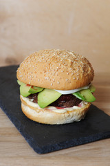 Burger closeup on a slate base, glass and cutlery served on a wooden board