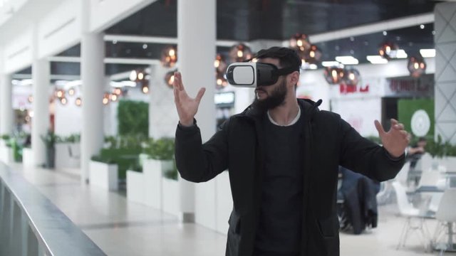 Young Man using virtual reality goggles in shopping center, blurred background