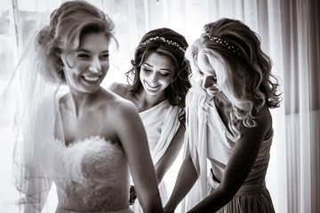 Naklejka premium Bride laughs while bridesmaids button up her corset before the w