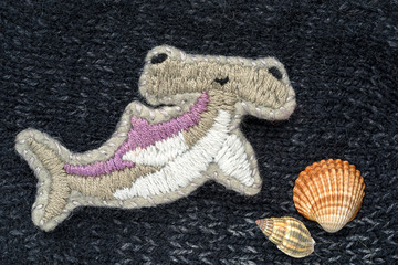 hand embroidered brooch in the form of a hammer fish and sea shells on a crafts knitting background