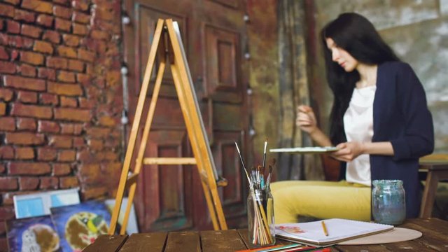 Young woman artist draw pictrure with watercolor paints and brush on easel canvas