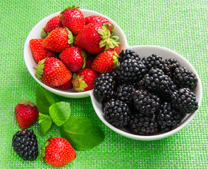 strawberries and blackberries in a white ceramic cups on a green cloth