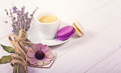 Obraz na płótnie Canvas Cup of coffee with two macarons, bunch of lavender and wooden heart. Violet and purple concept on white background