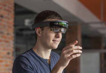 Young man wearing virtual reality goggles. Headset. Glasses with virtual screen. Man touch something using modern glasses with virtual screen. Device.  Man playing game.
