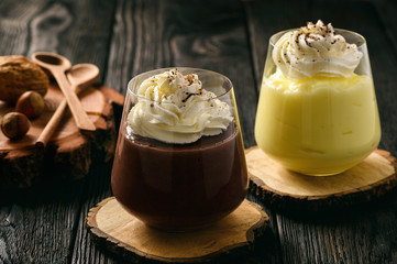 Cream and chocolate pudding with whipped cream on wooden background.