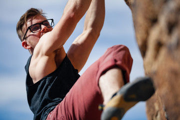 Fototapeta premium Young caucasian man wearing glasses climbs a granite cliff in the desert