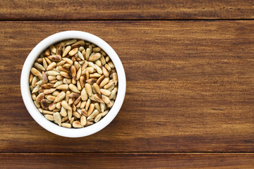 Roasted sunflower seeds in small bowl, photographed overhead on wood with natural light