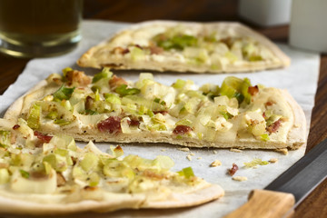 Homemade leek and bacon tarte flambee, a traditional French and German oven baked pizza-like pie, photographed with natural light (Selective Focus on the front of the middle slice)