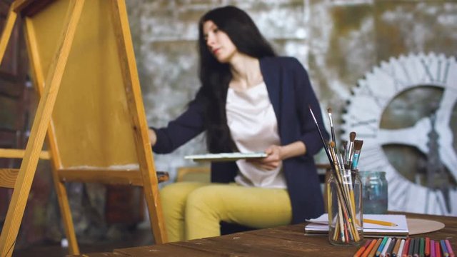 Young woman artist draw pictrure with watercolor paints and brush on easel canvas