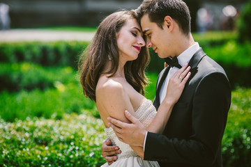 Bride and groom lean to each other tender standing among green b