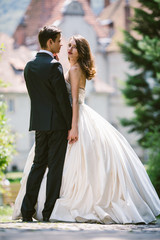 Bride in luxurious ivory dress looks over groom's shoulder while