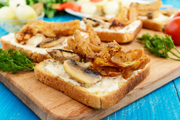 Crispy toasted white bread in the shape of a square with mushrooms, onions, french fries, tartar sauce on a cutting board on a blue wooden background.