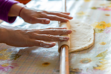 female hands rolling raw dough on white table