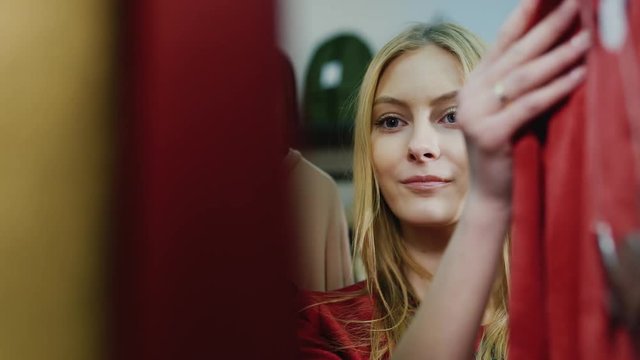 Young woman chooses a dress in a store. Portrait seen through the clothes, she goes through dress on a hanger