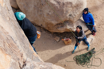 Young african american woman climbs along a granite cliff in the desert dressed for cold weather while friends watch
