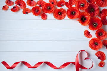 Wooden background with red poppies flowers and ribbon in the shape of heart