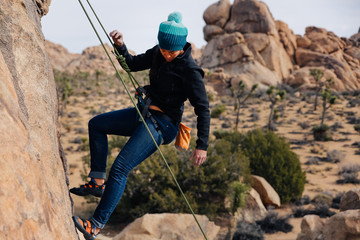 Young african american woman climbs along a granite cliff in the desert dressed for cold weather