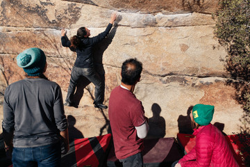 Young caucasian woman climbs along a granite cliff in the desert while her friends nearby watch